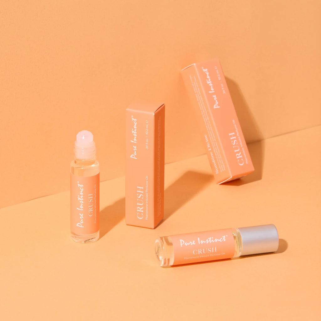 Pheromone roll-on perfume bottle with silver cap and orange boxes, angled view