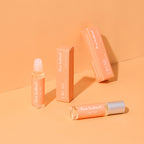 Pheromone roll-on perfume bottle with silver cap and orange boxes, angled view