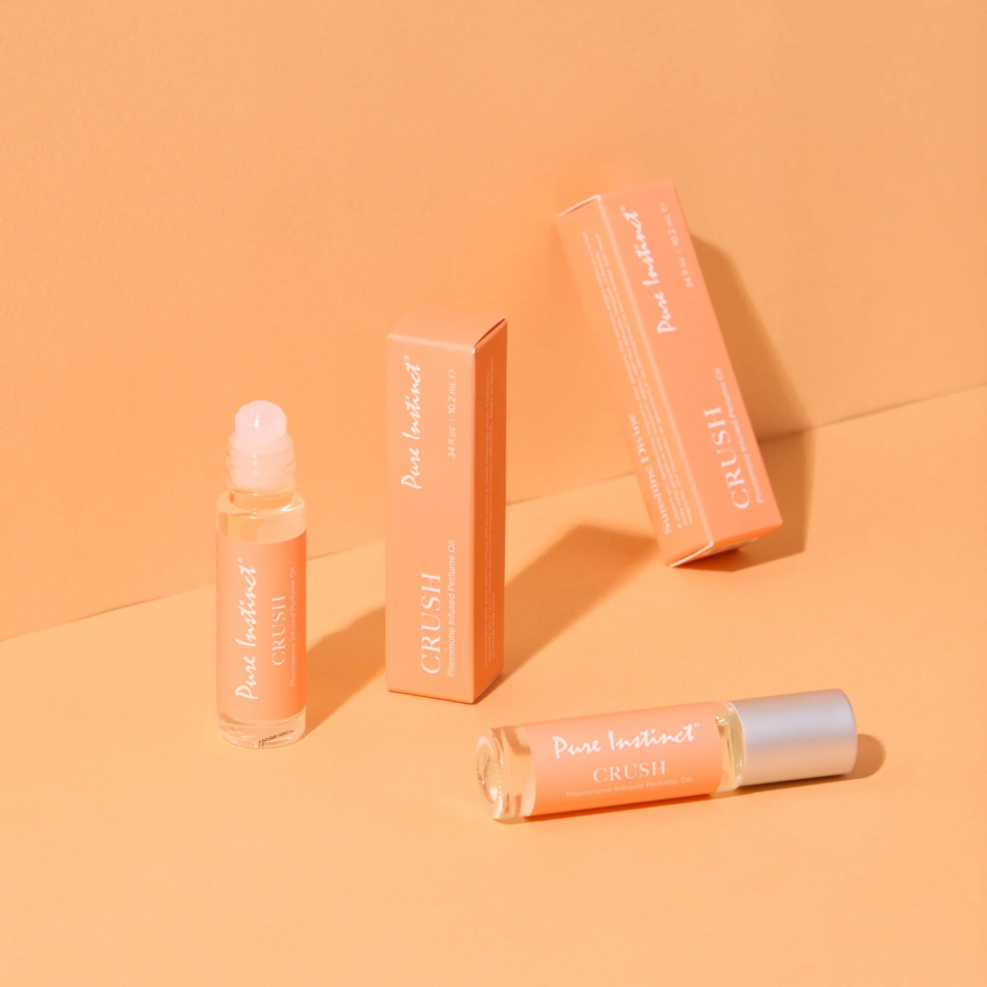 Pheromone roll-on perfume bottle with silver cap and orange boxes, angled view