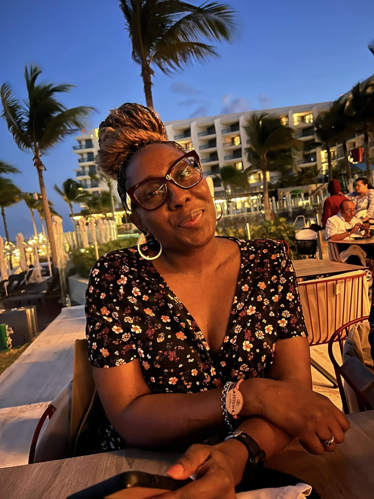 Woman sitting outdoors with palm trees and a building in the background