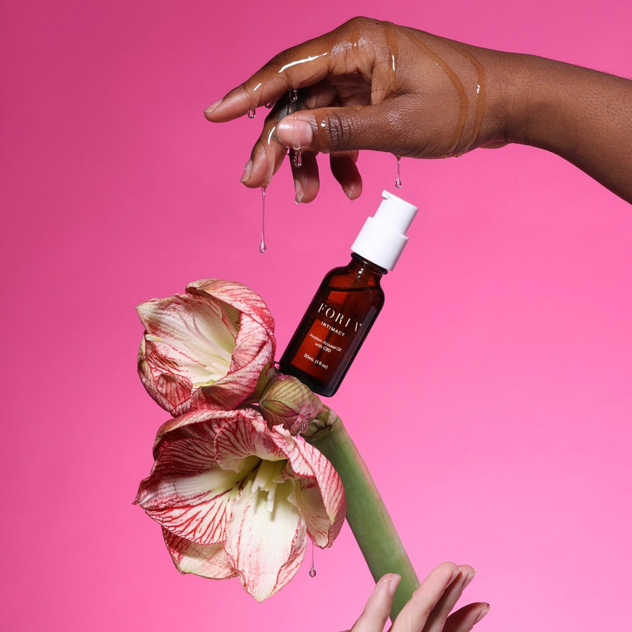 CBD arousal oil bottle with dropper, held over floral petals