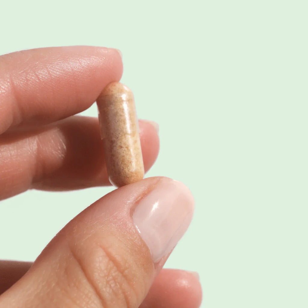 Vaginal suppository capsule held between fingers, tan colored