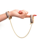 Pair of rhinestone handcuffs on wrists connected by gold chain