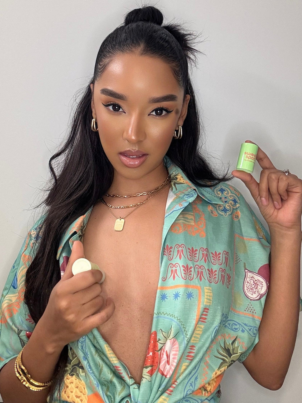 Green roll-on fragrance stick held in hand near a person wearing jewelry
