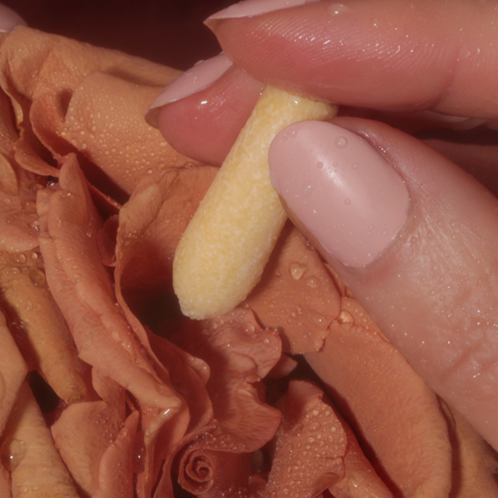 Yellow CBD suppository held between fingers close-up