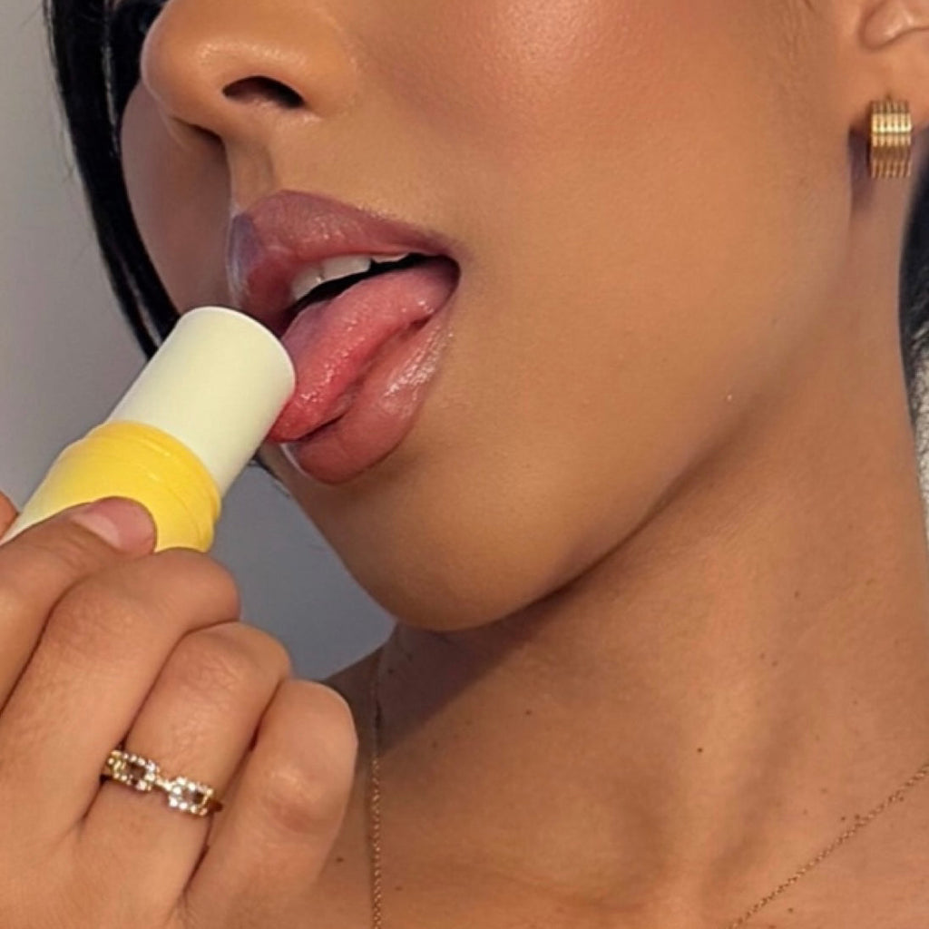 Solid fragrance stick applied to lips, pale yellow balm with white cap