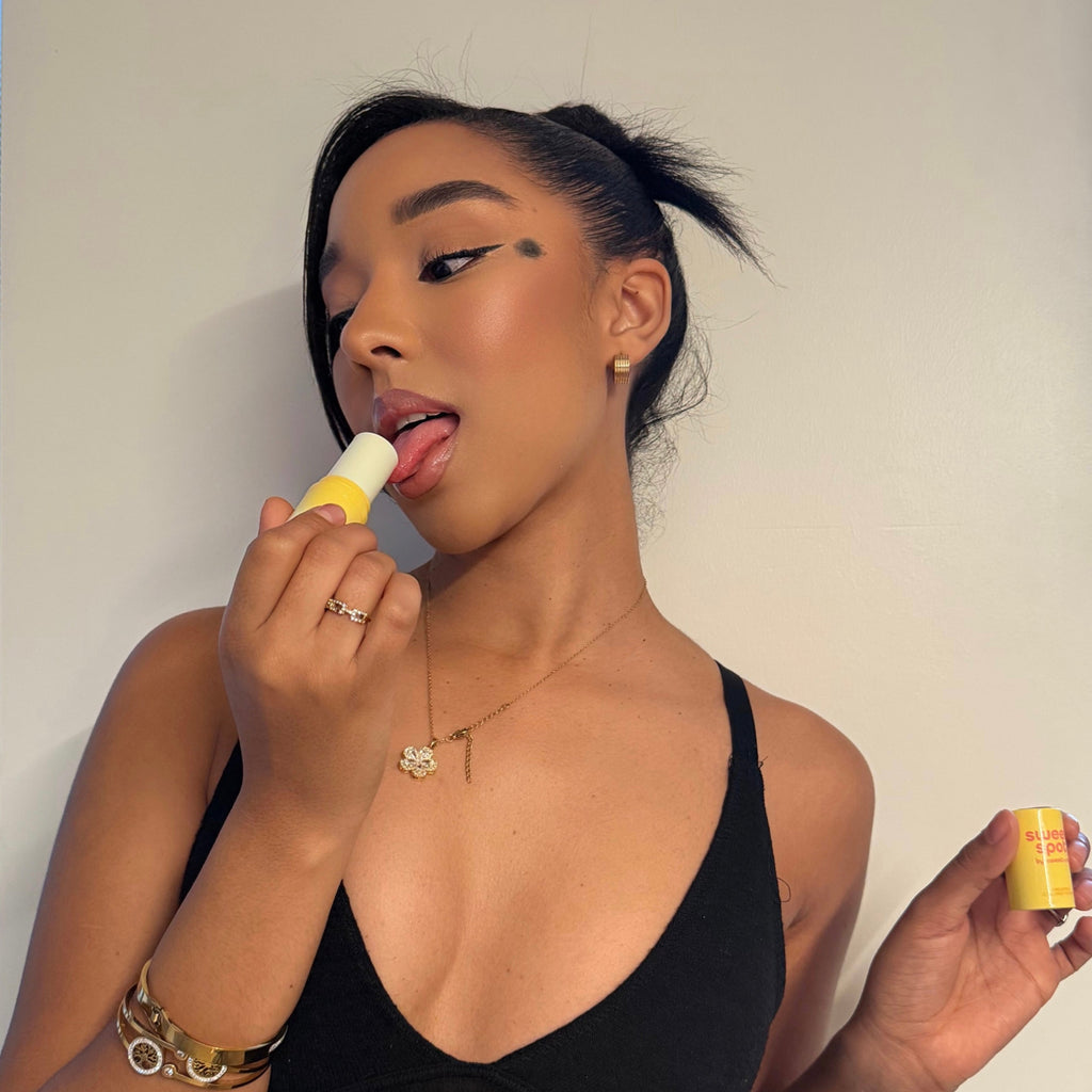 Solid fragrance stick applied on lip by model, yellow tube held near face.