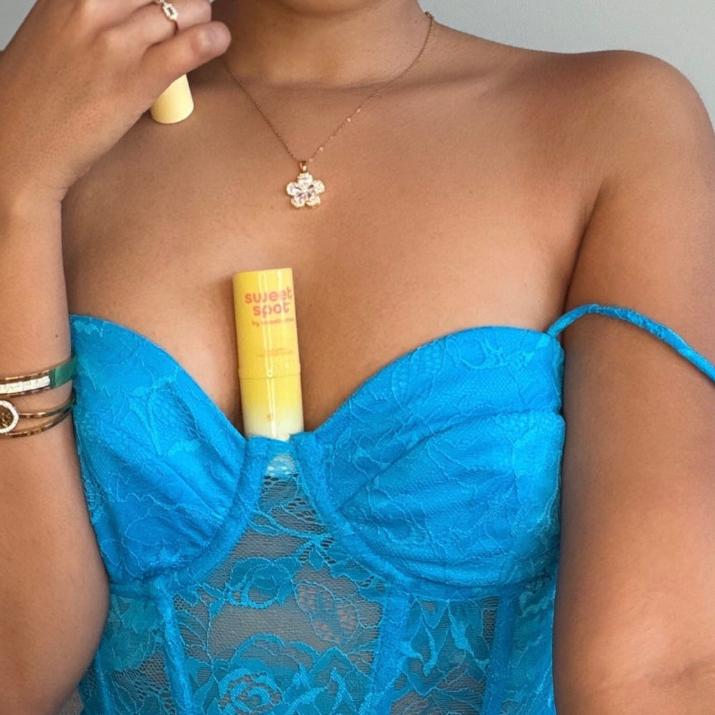 Solid fragrance stick held against blue dress neckline, pale yellow balm with white cap