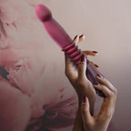 Pink thrusting vibe held in hand with ribbed handle and rounded tip.