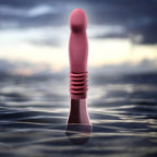 Pink thrusting vibe with ribbed handle and rounded tip standing in water.