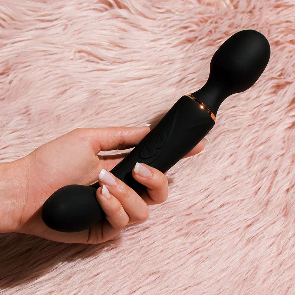 Dual-ended vibrator held in hand with dark silicone and rose-gold detail band