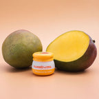 Sweetums mango flavored lip balm jar beside mango halves