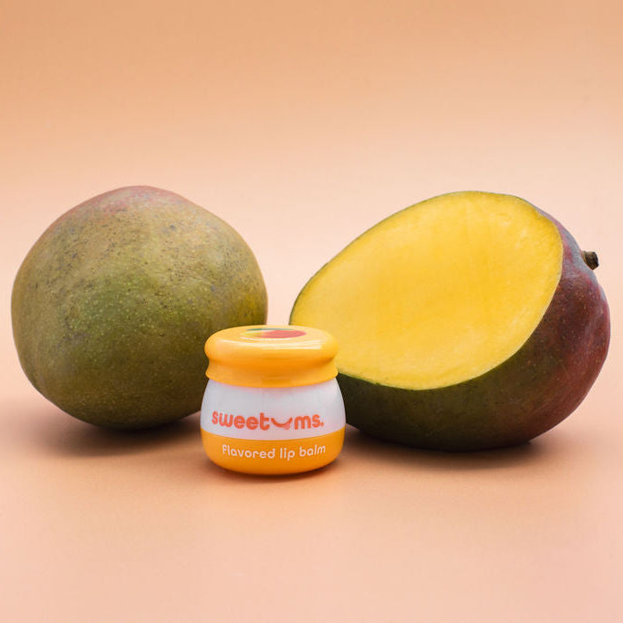 Sweetums mango flavored lip balm jar beside mango halves